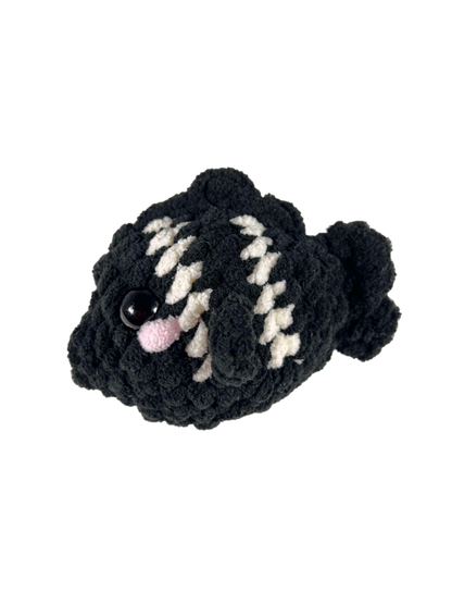 Black crochet fish plushie with 2 white stripes facing left.