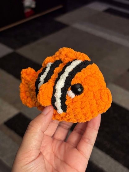 Orange crochet fish plushie with 2 white and black stripes being held.