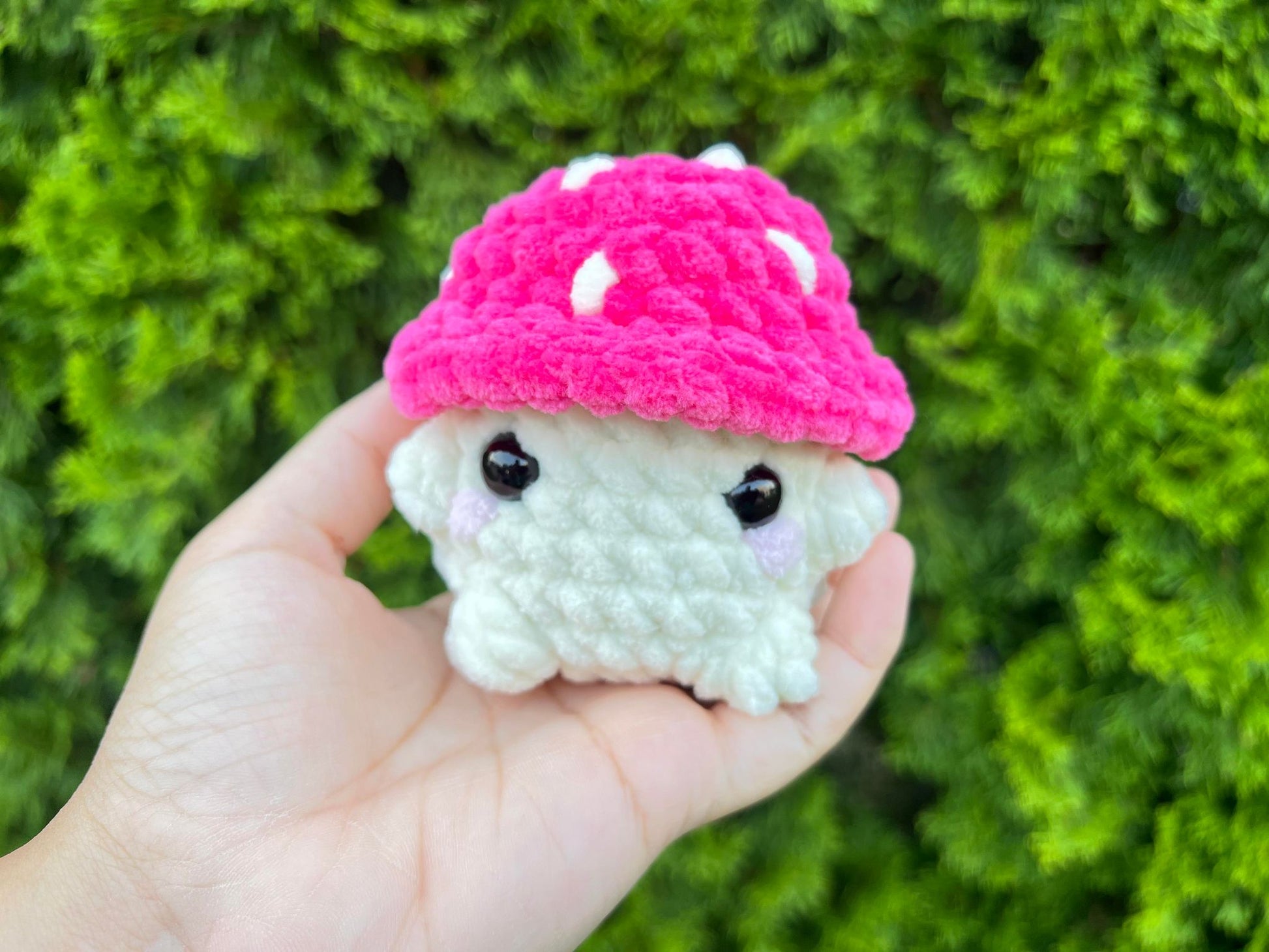 Pink crochet mushroom sitting looking forward in a garden.