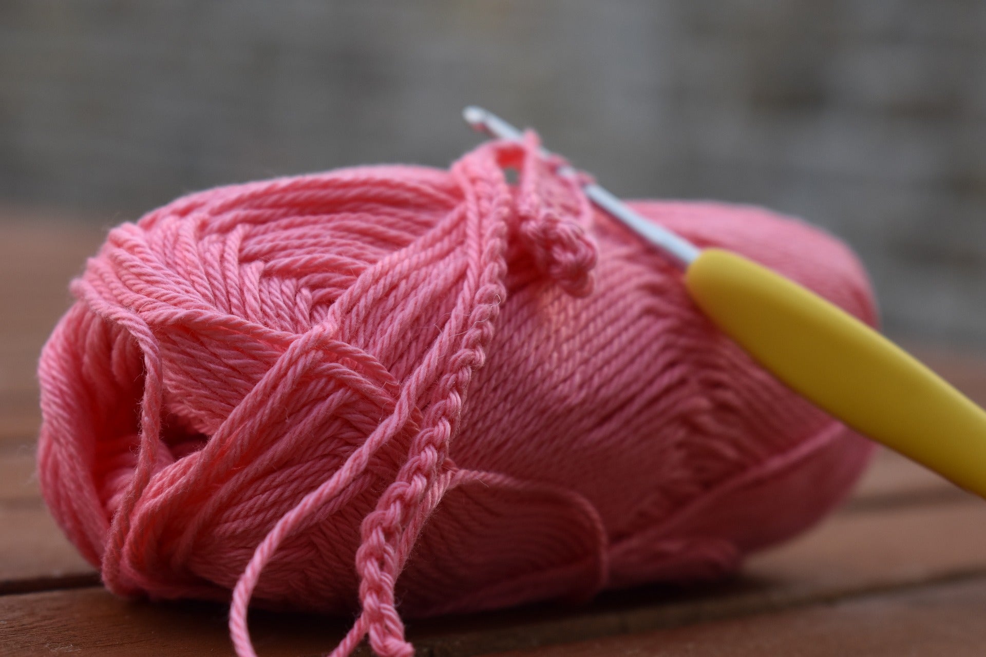 A ball of pink yarn that is being crocheted with a yellow hook.